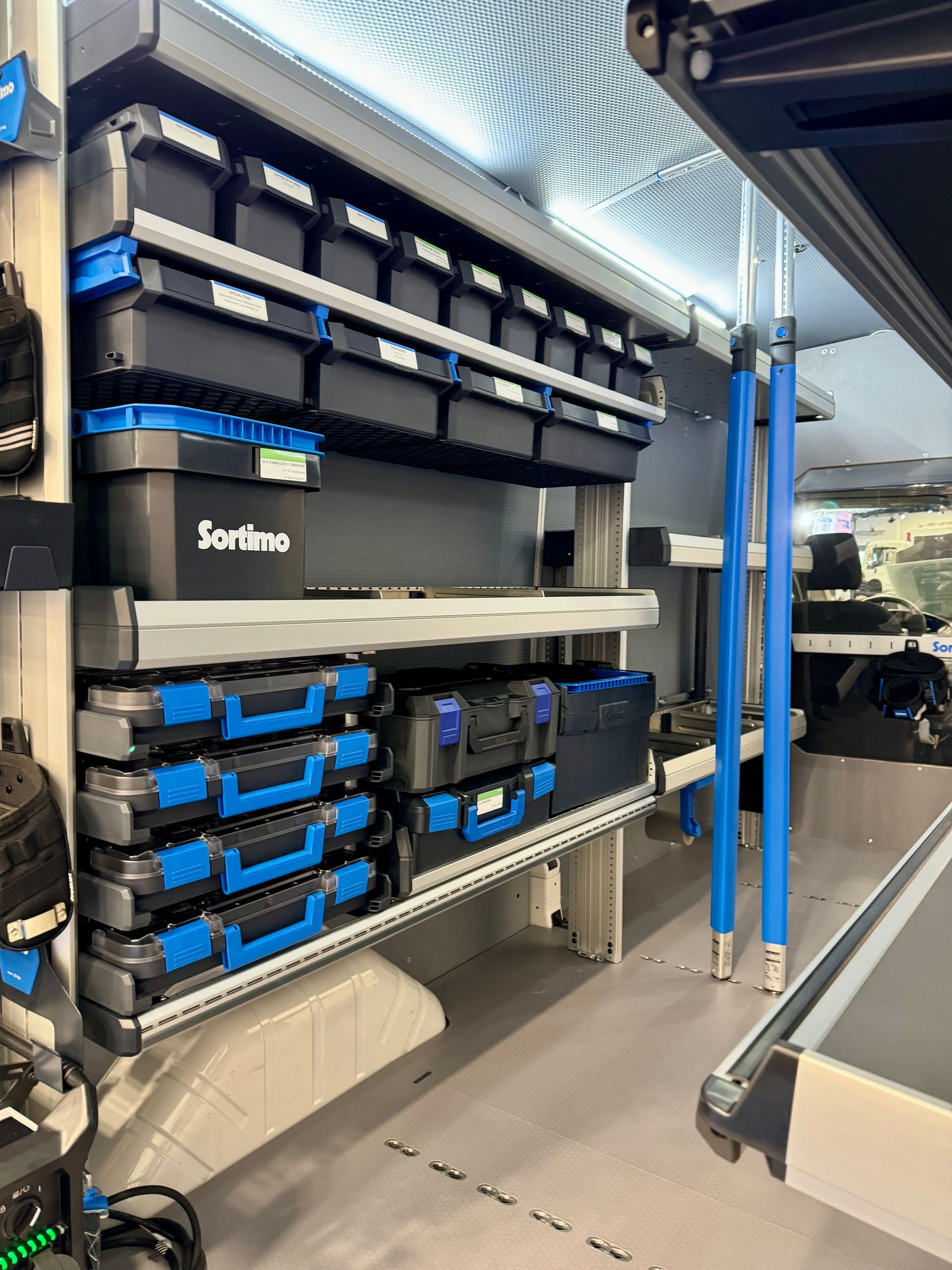 Interior of a van with shelving and storage containers, mostly black and blue.