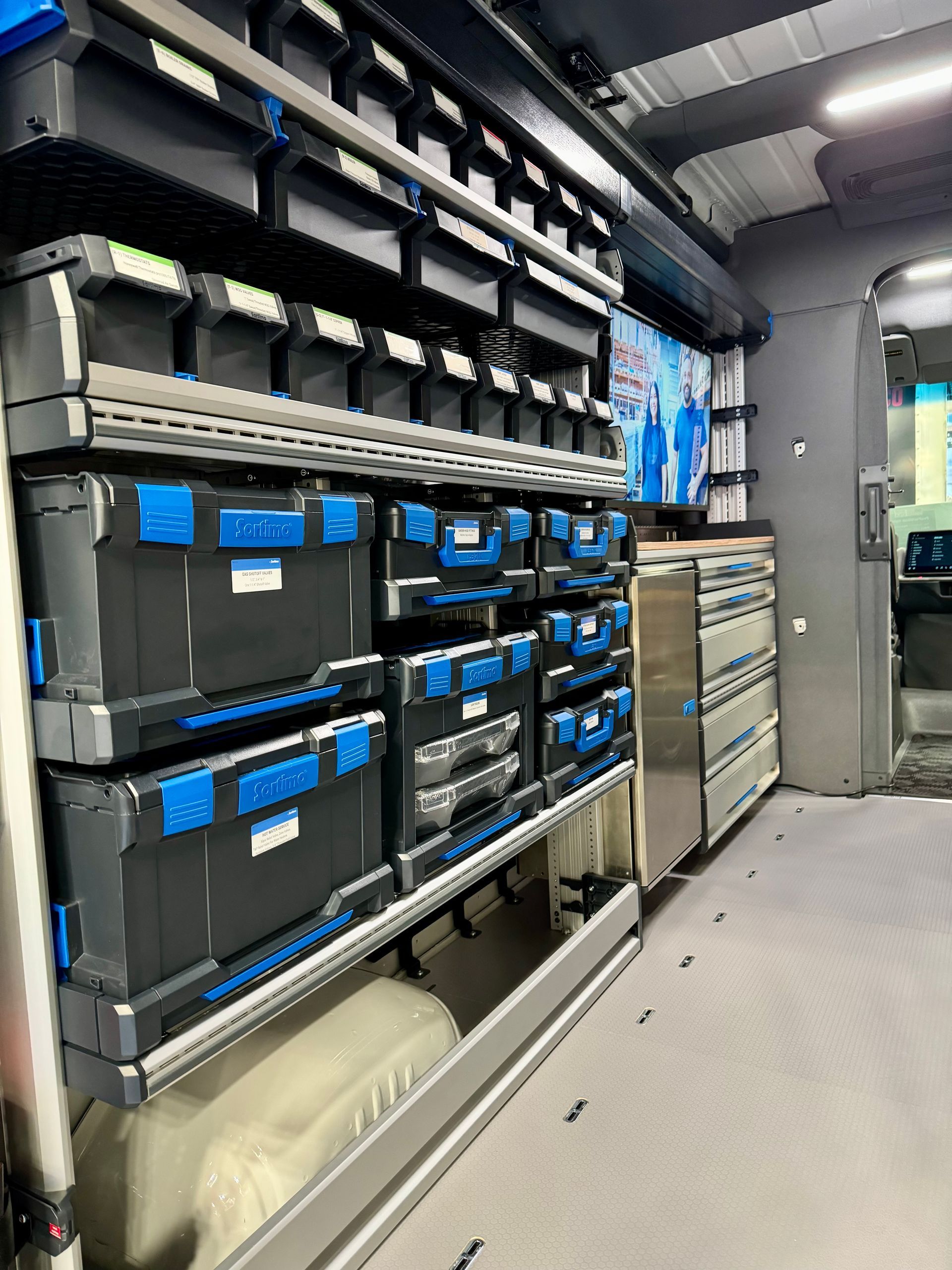Van interior with black and blue storage bins on shelves, alongside a metal cabinet.