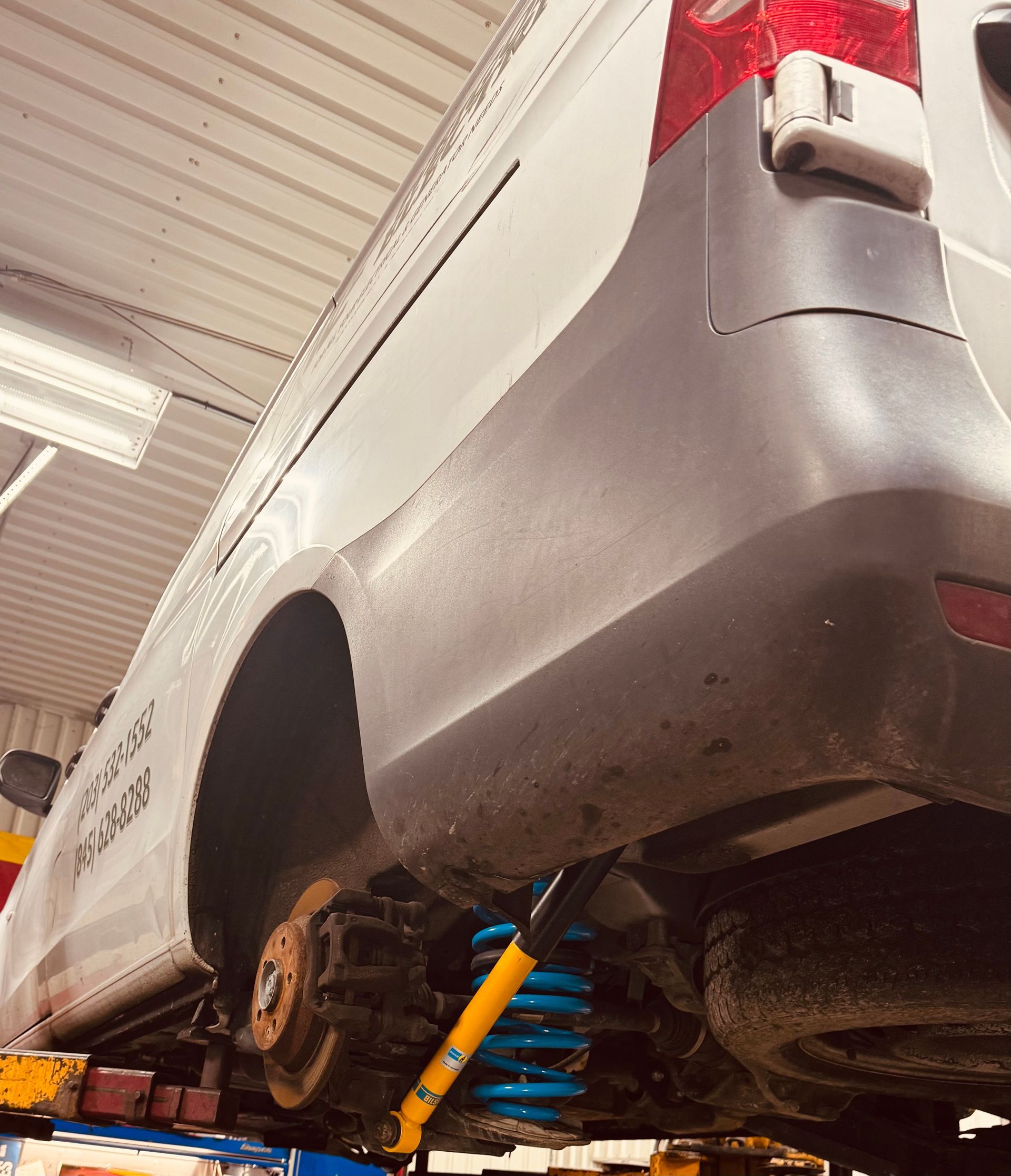 Van's rear end raised on a lift for service, revealing a shock absorber and suspension components.
