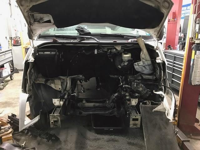 Bare vehicle frame in a repair shop, raised on a lift; wheels are visible.