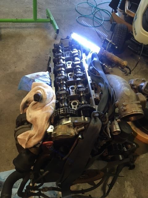 White truck cab mounted on a chassis in a workshop. A person stands in the background doorway.