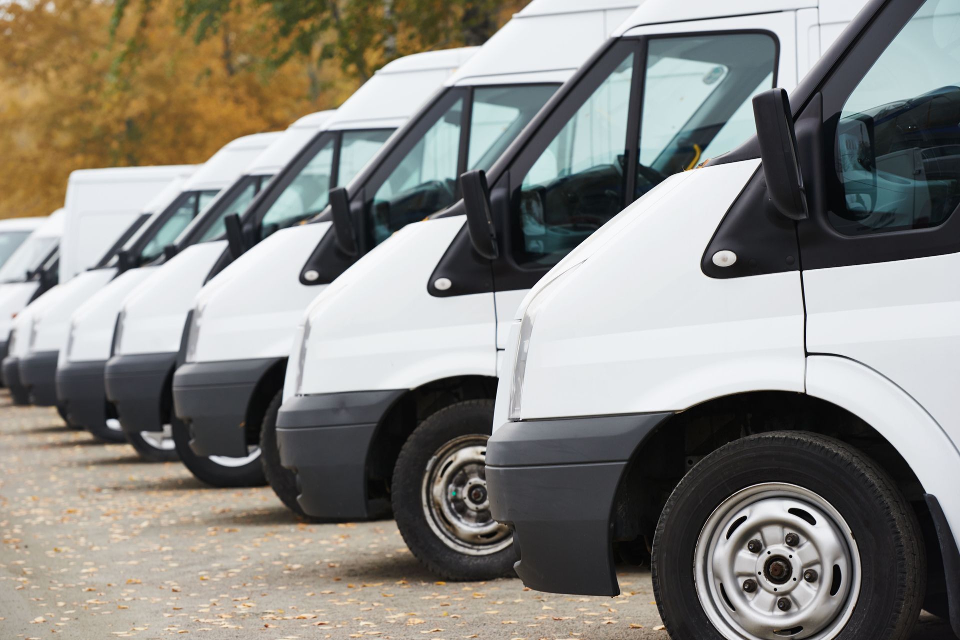 A row of white vans parked next to each other in a parking lot.