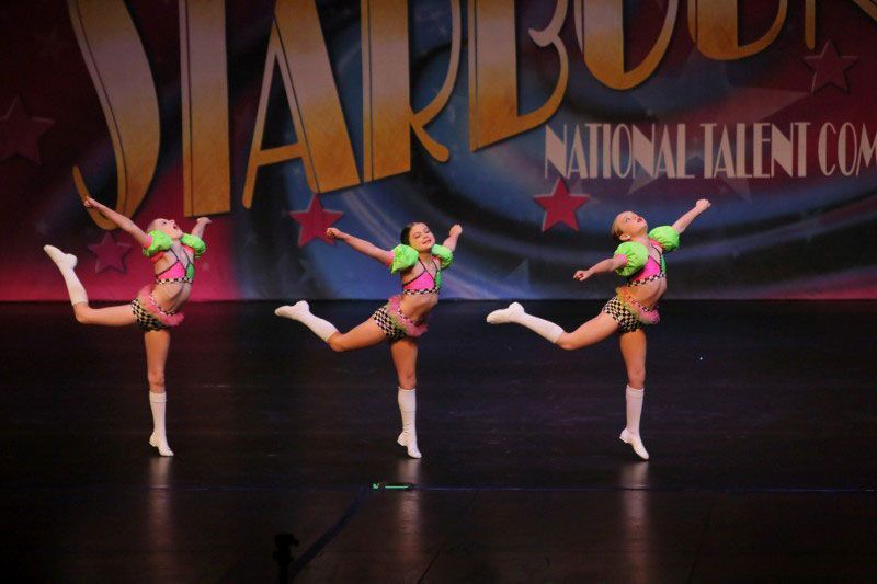 Three young dancers on stage in colorful costumes.