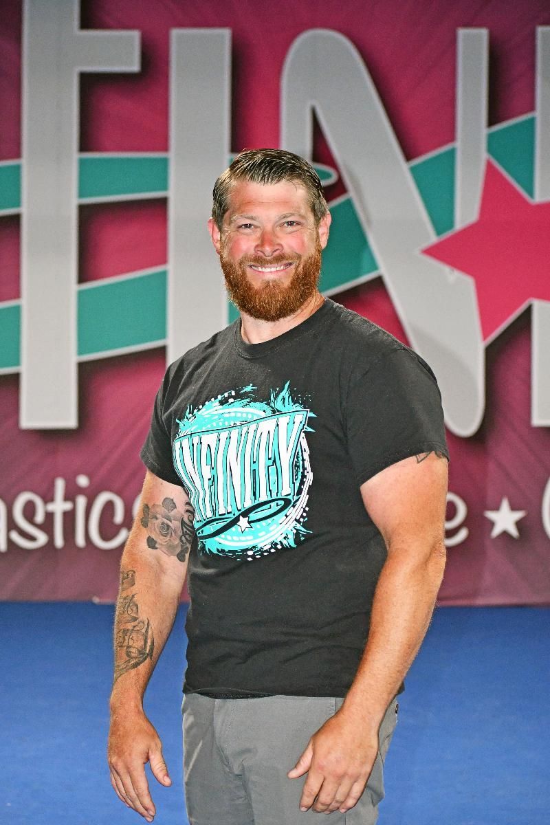 Man with beard and tattoo stands in front of a pink banner.