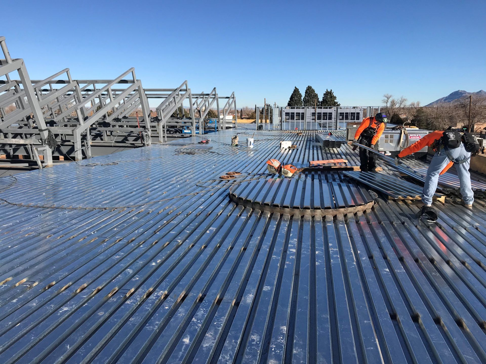 Workers on a metal roof, installing sections. Bright sunlight. Construction site, outdoors.