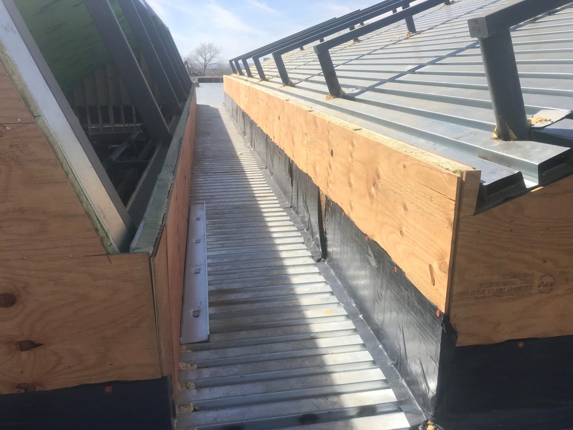 A narrow metal-lined trough between two slanted metal roofs, framed by plywood.