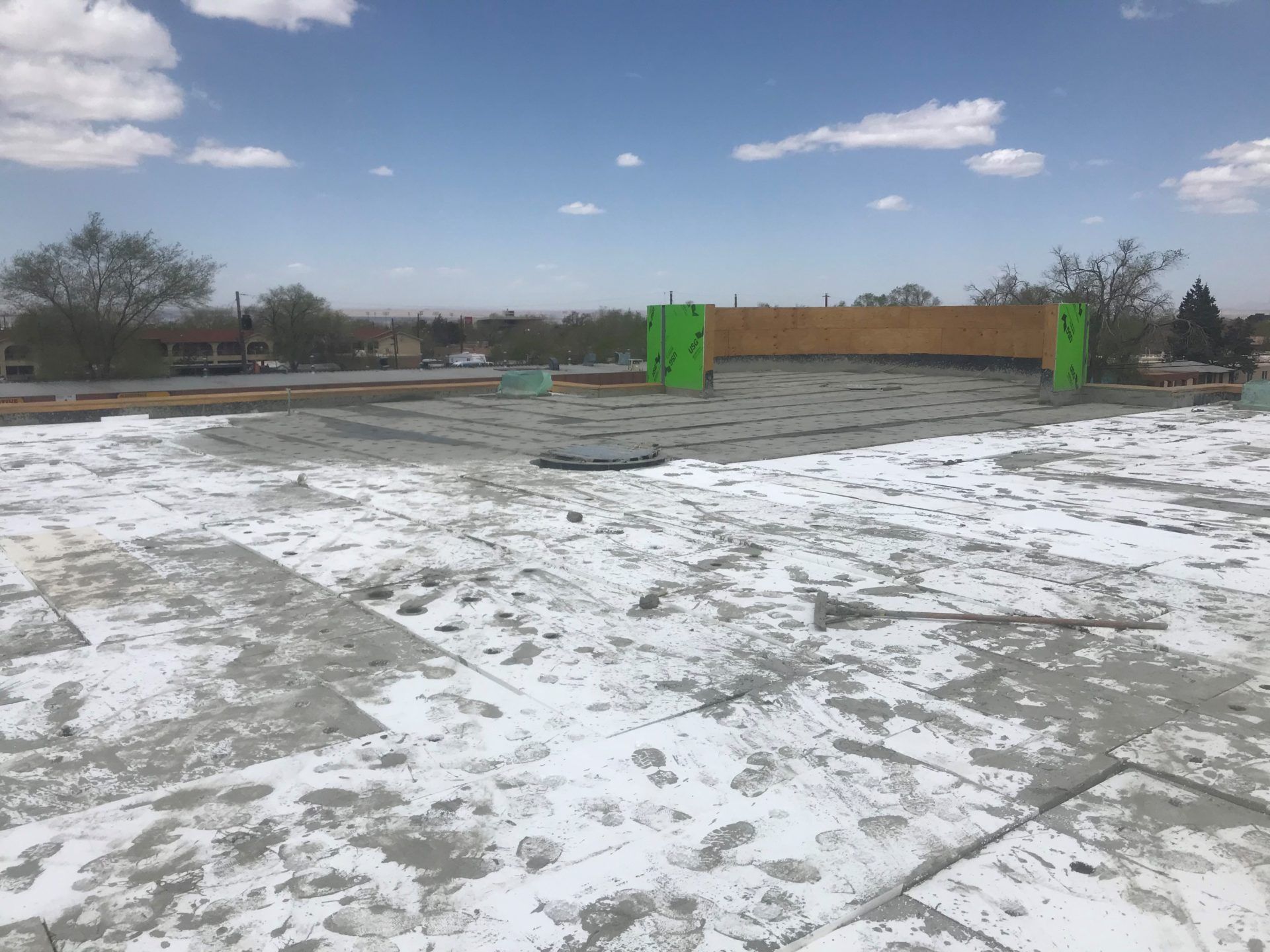 Flat roof under construction with gray and white materials, wooden beams, green supports, and a blue sky.