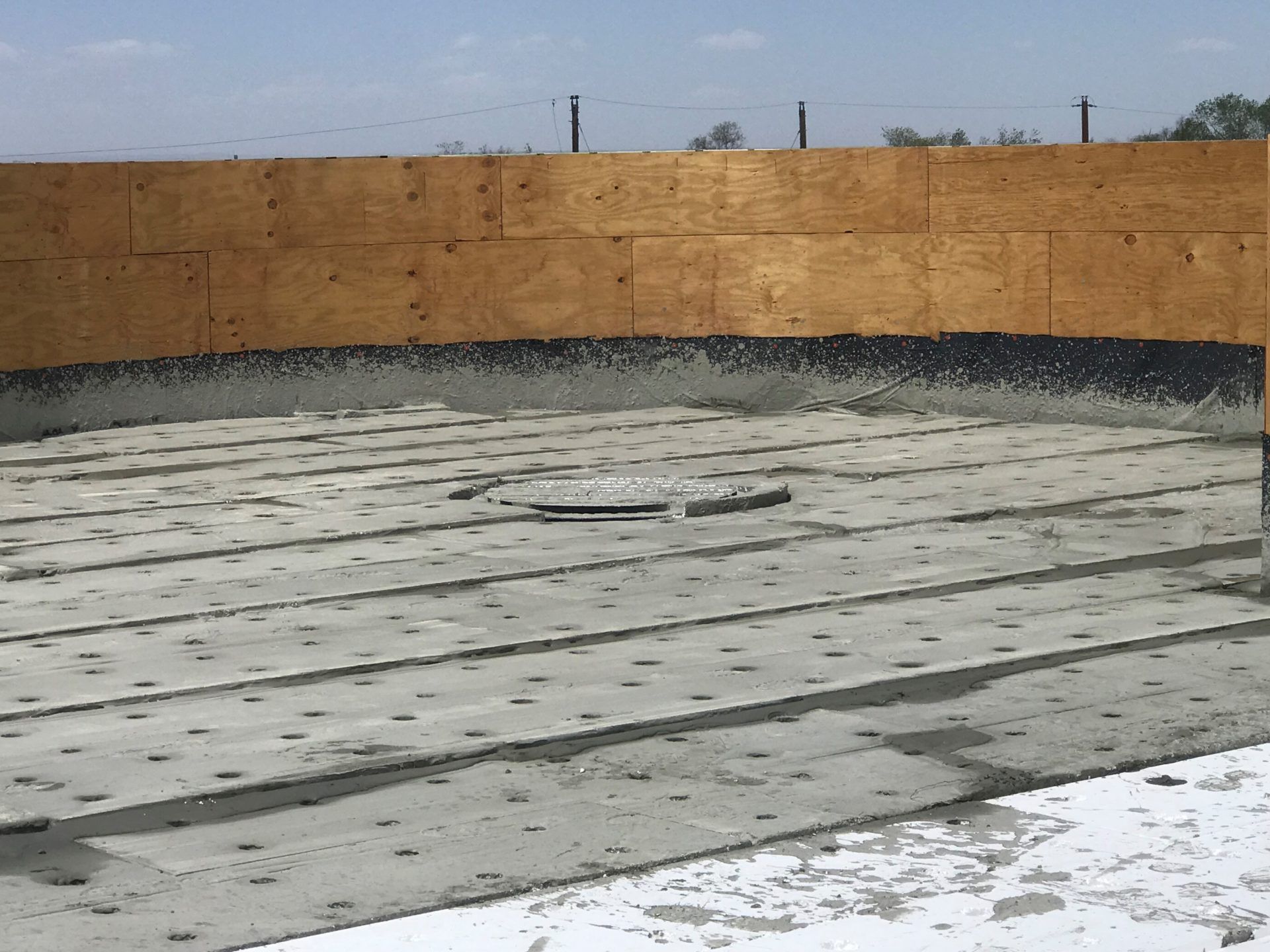 Concrete floor with a central drain, black edging, and wooden fence in the background.