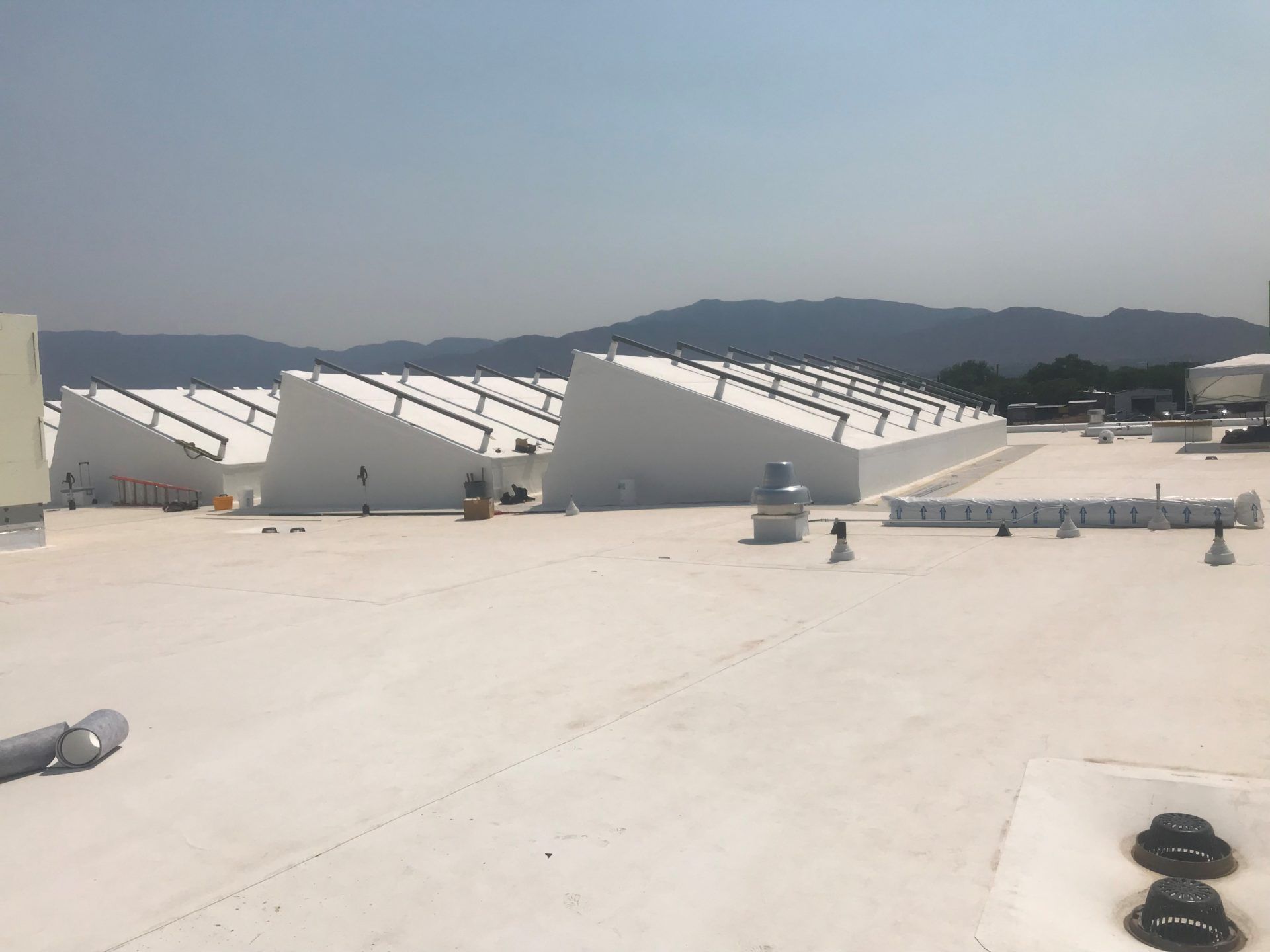 White commercial building roof with multiple sawtooth skylights; mountains in the background.