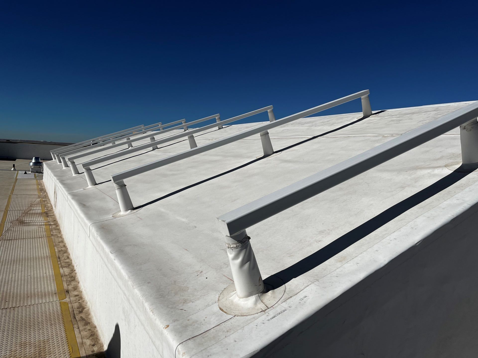 Rooftop with white surface, supporting metal rails. Blue sky in the background.