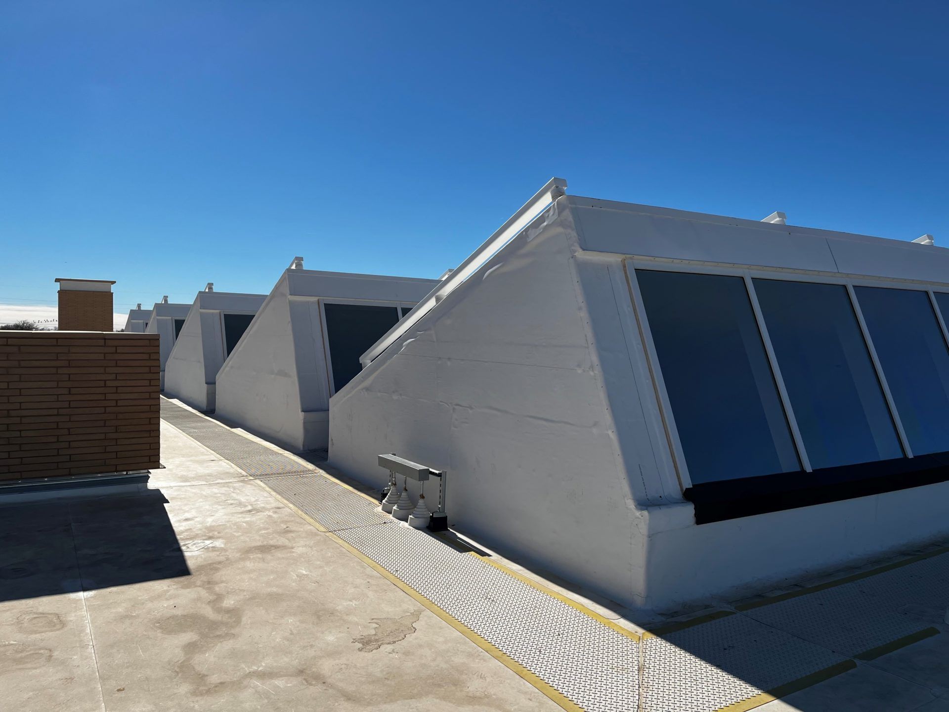 White slanted roof structures with large tinted windows on a flat roof under a blue sky.