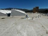 Flat white roof of a commercial building with angled skylights. Tower and mountains in background.