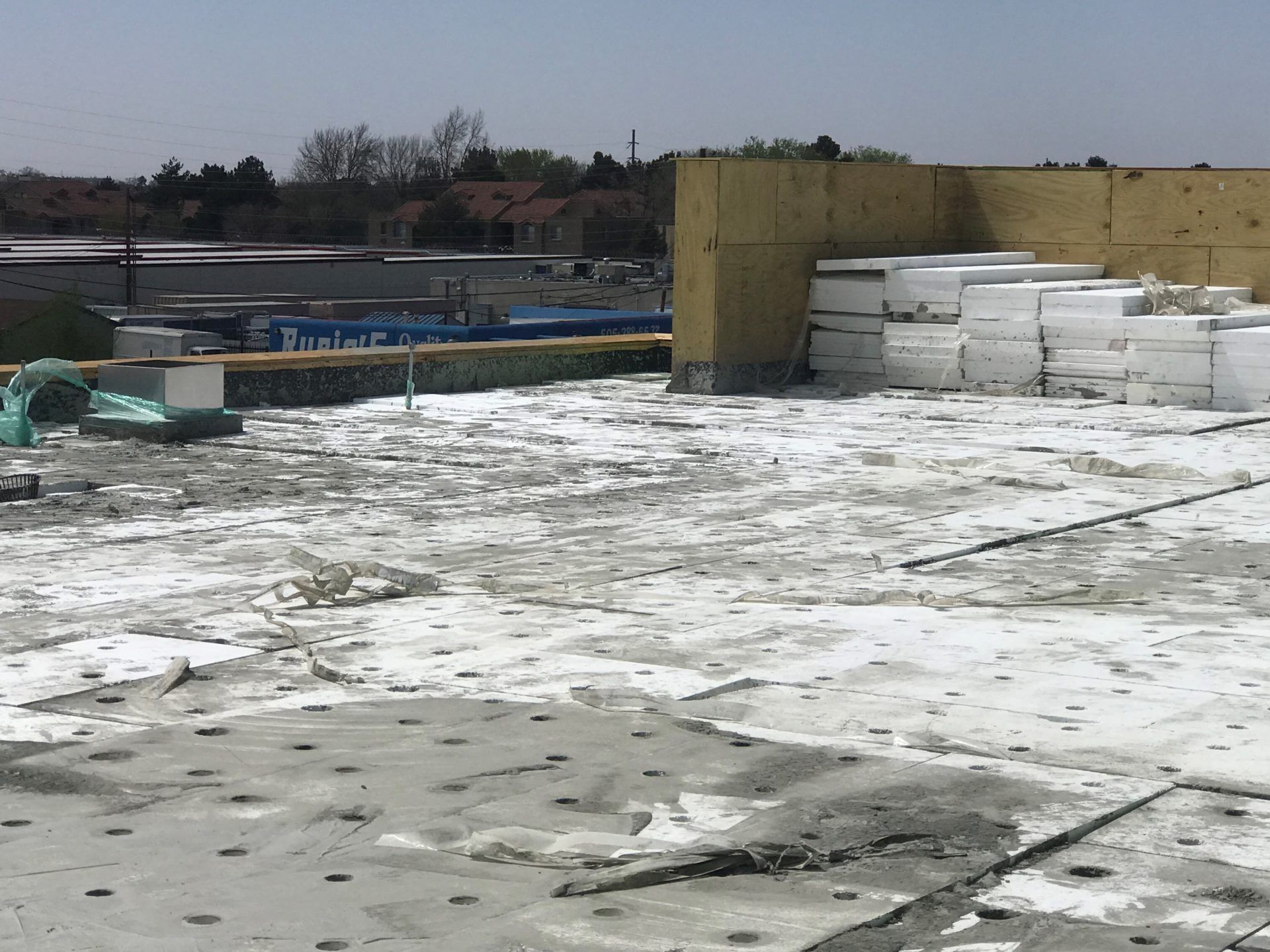Rooftop under construction with concrete base, insulation panels, and supplies.