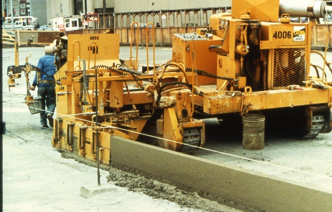 Yellow concrete curb machine shaping fresh concrete curb; construction site.