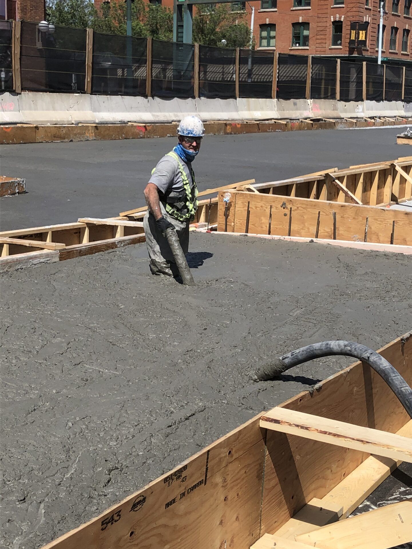 Construction worker in concrete, leveling it with his feet, wearing safety gear.