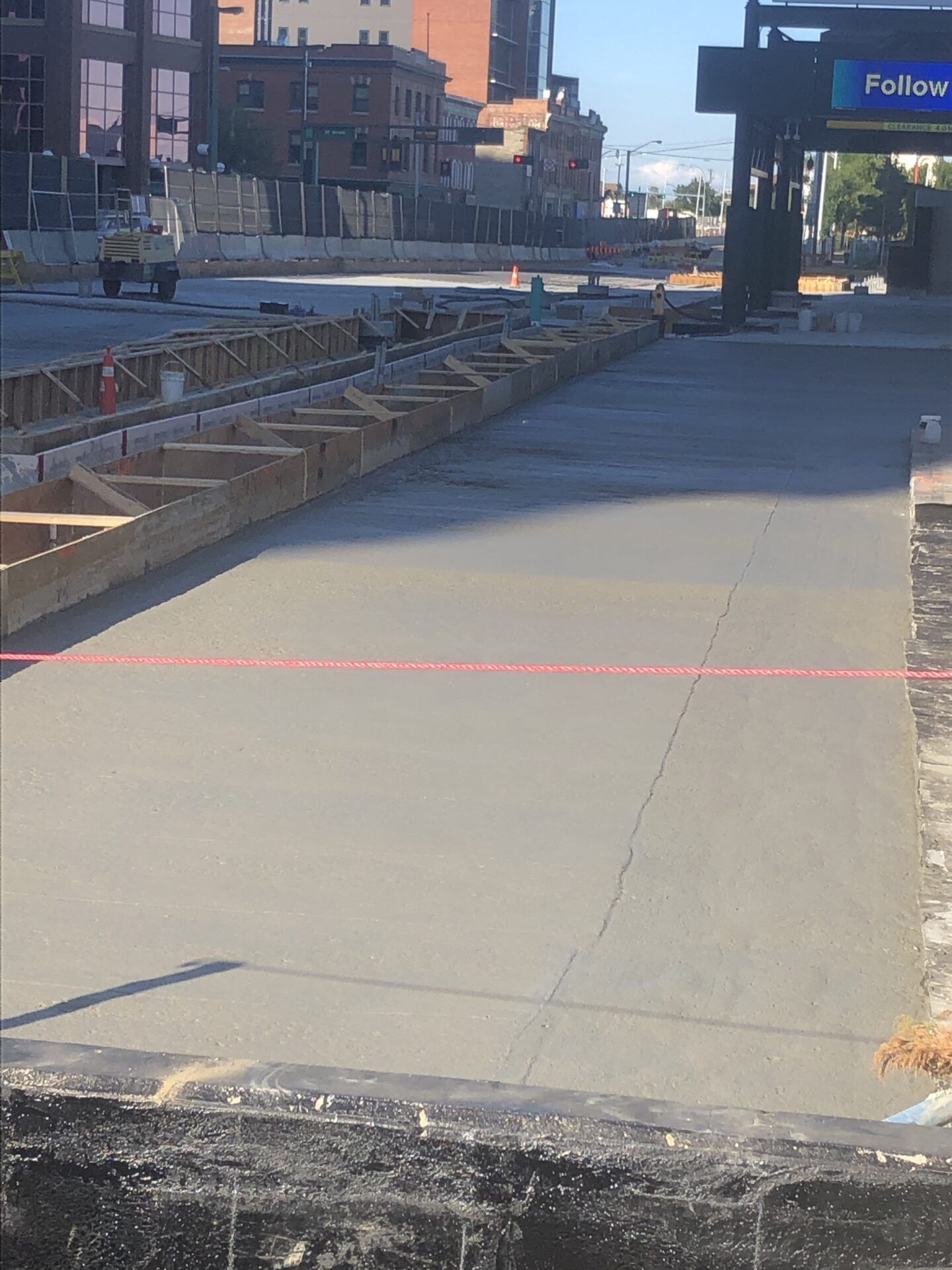 Construction site with freshly poured concrete, wooden forms, and city buildings in the background.