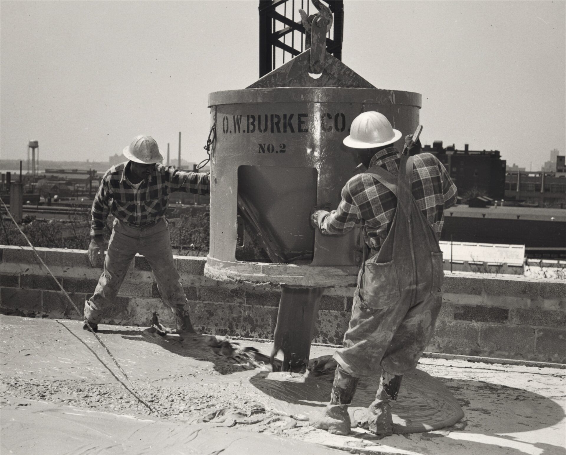 Two construction workers guide a concrete bucket, on a sunny day.