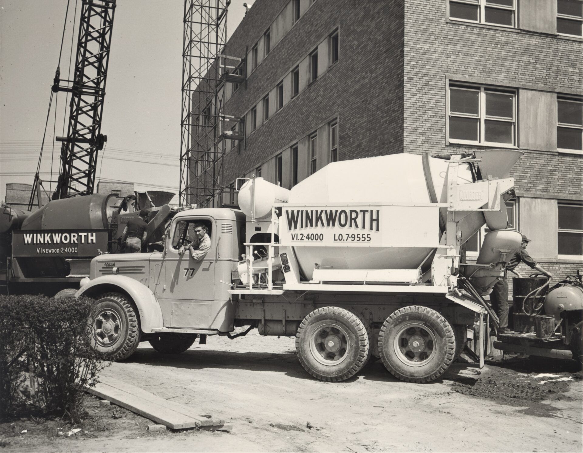 Two Winkworth concrete trucks at a building construction site. A worker stands near the truck, and another sits inside.