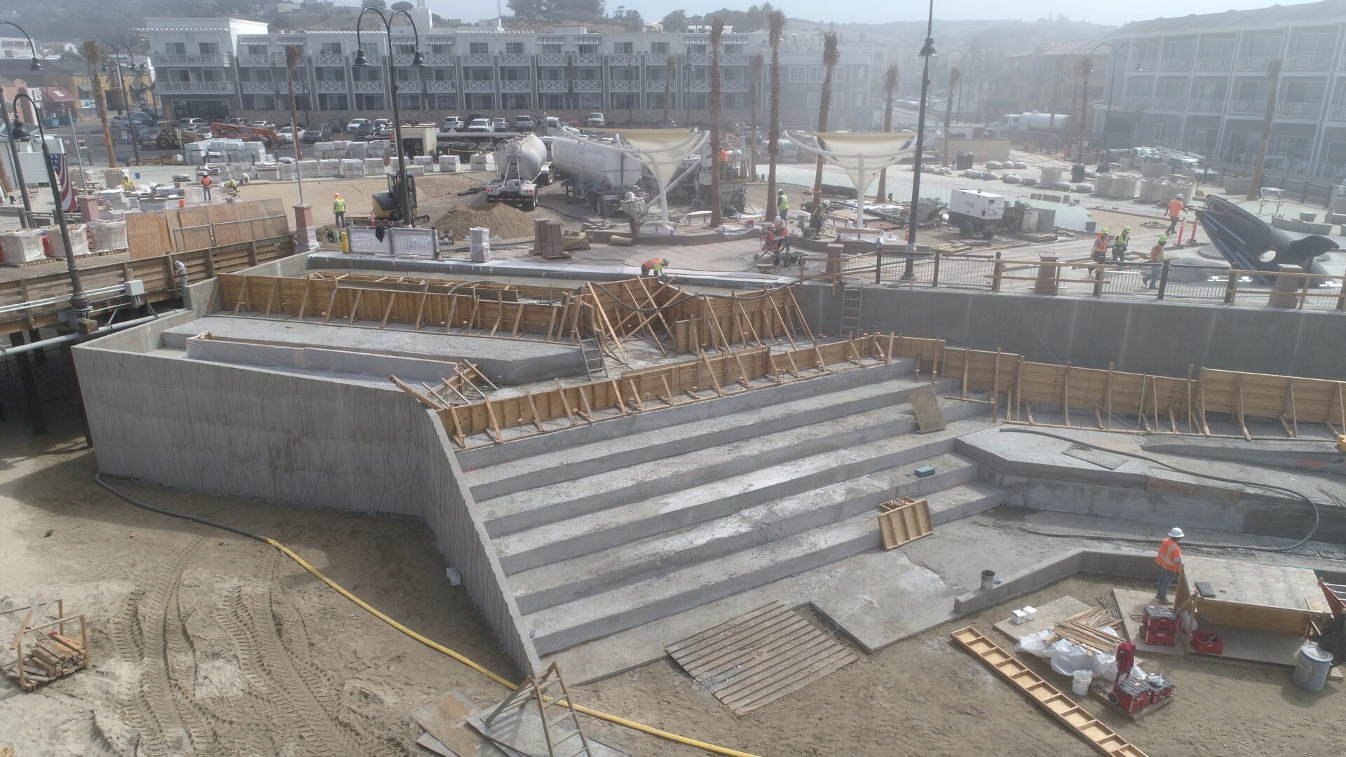 An elevated view of a concrete tiered seating structure under construction, surrounded by dirt and building materials.