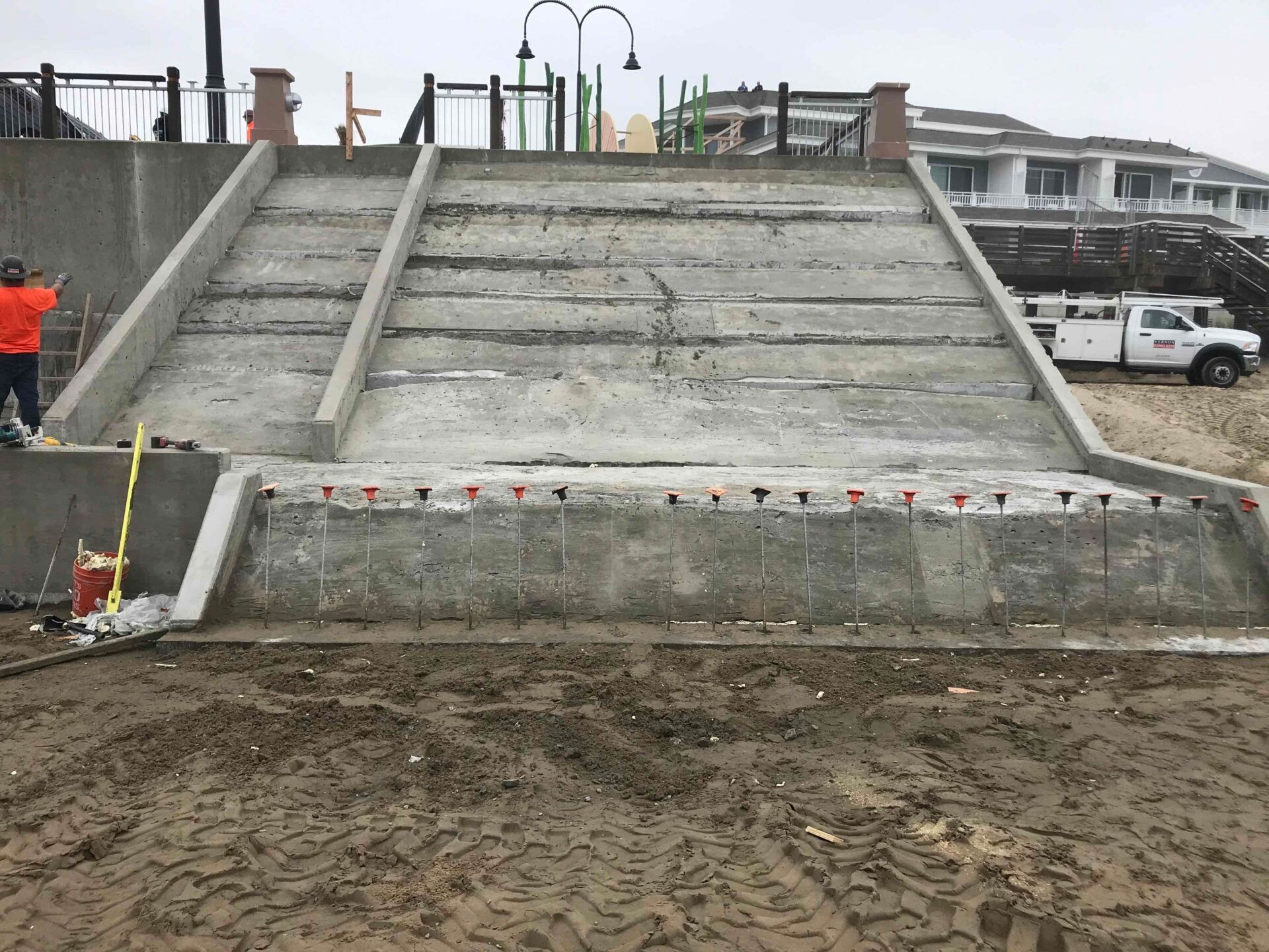 Under-construction concrete stairs leading from a beach area up to a walkway with a utility truck parked in the background.