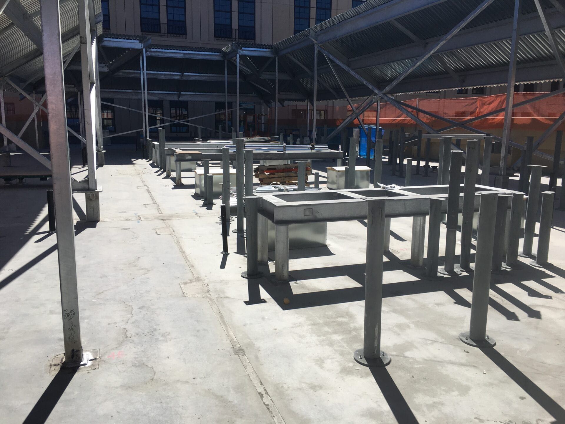 A construction site with metal structural supports and box-shaped vents installed on a gray concrete surface.