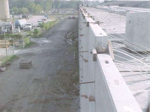 A high-angle view of a concrete retaining wall under construction alongside a dirt road and construction site.