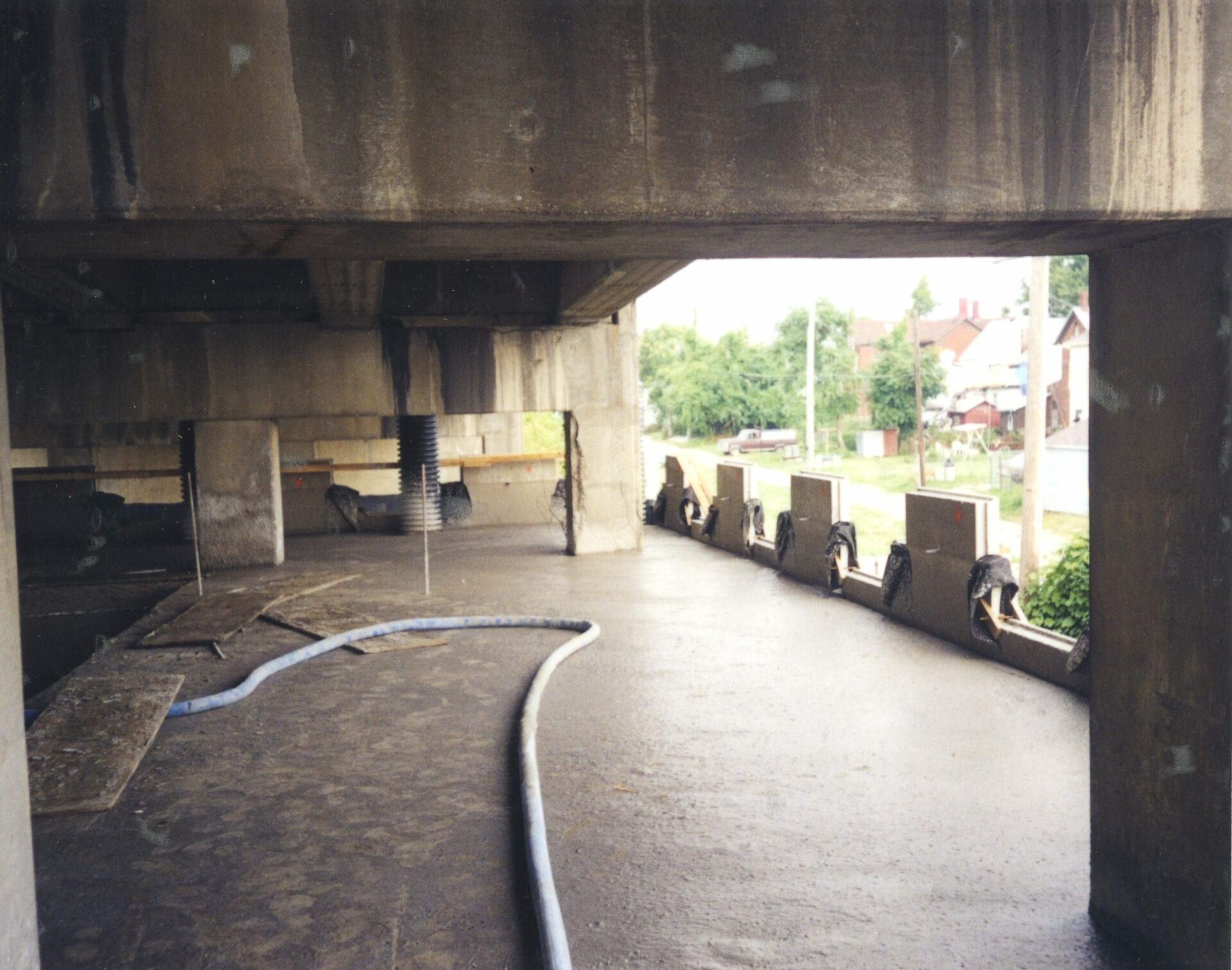 Concrete construction site showing an open-walled indoor area with a long hose and partial railing on a sunny day.