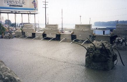 Freshly poured wet concrete covering a construction site with pipes spraying water and a billboard in the background.