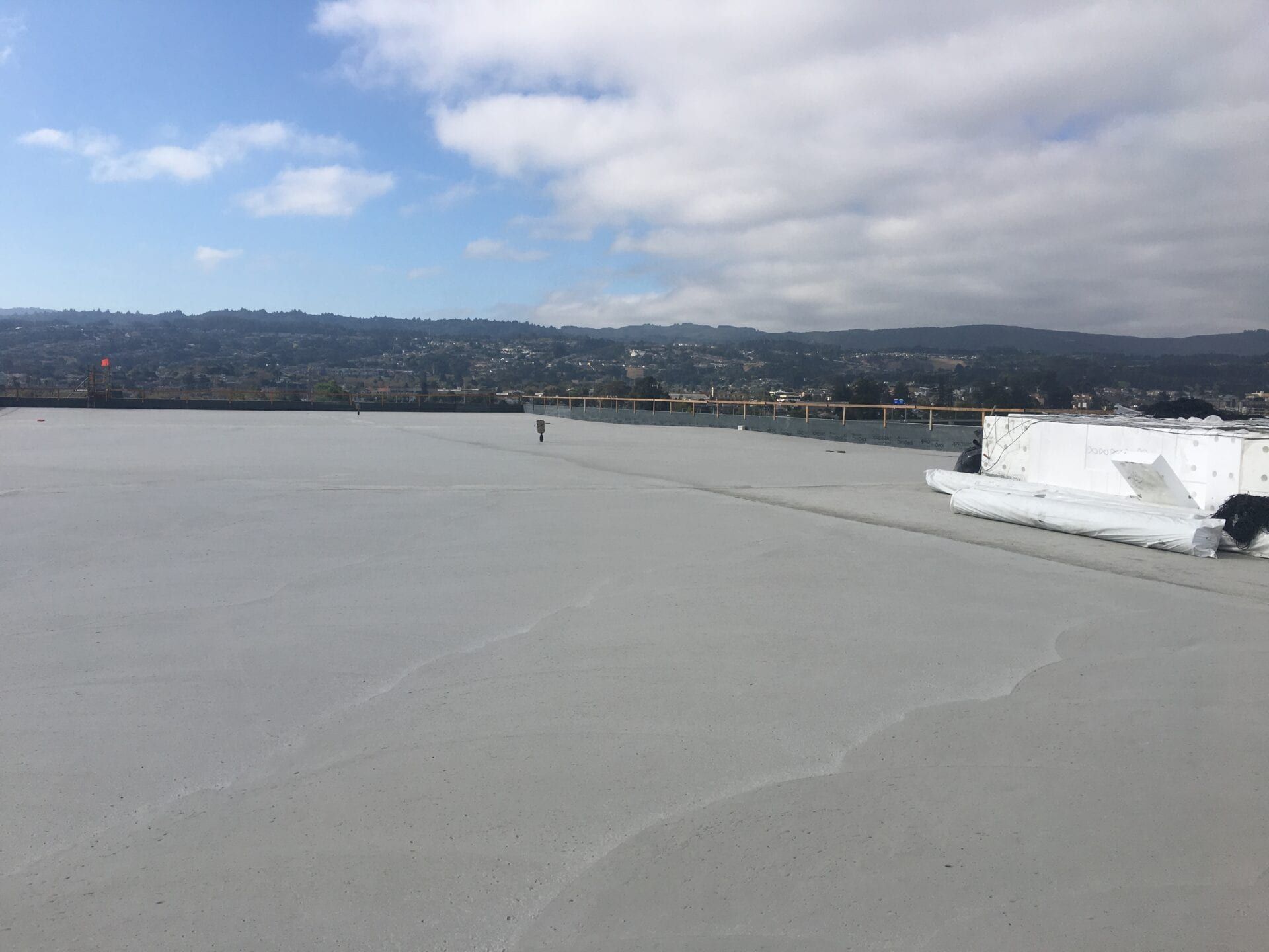 A flat, light gray roof surface under a cloudy sky, with distant hills and a white structure on the right side.