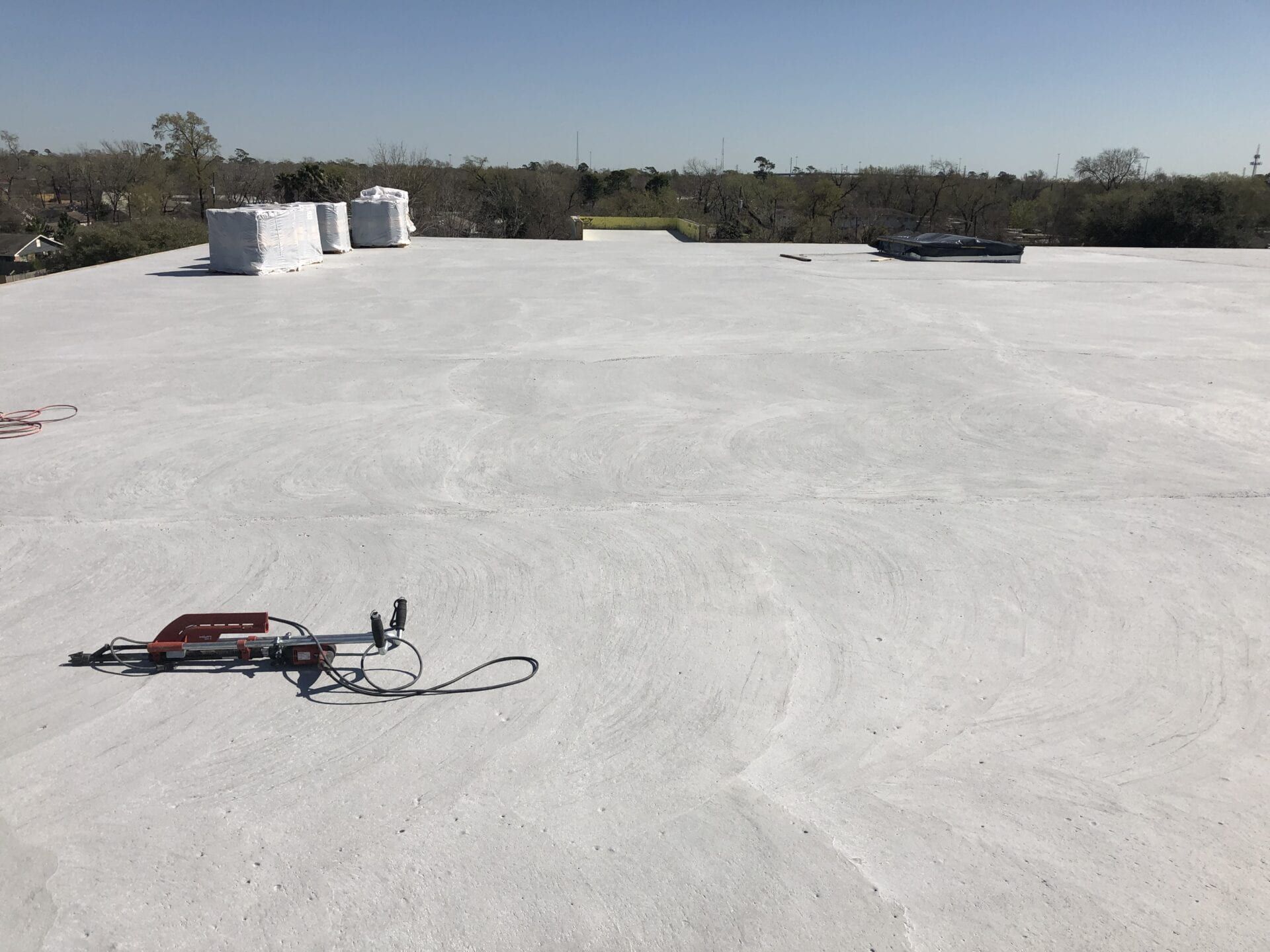 A wide view of a flat, white-coated commercial roof under a clear blue sky, with construction materials and equipment.