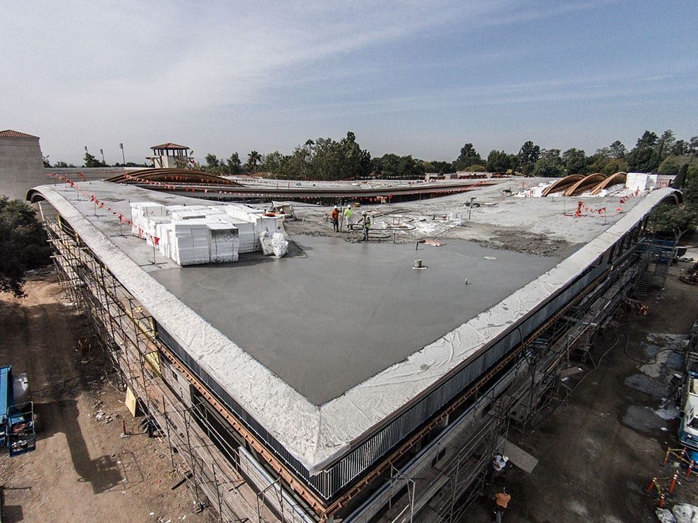 An aerial view of a building under construction, featuring a large, flat concrete roof surrounded by scaffolding.