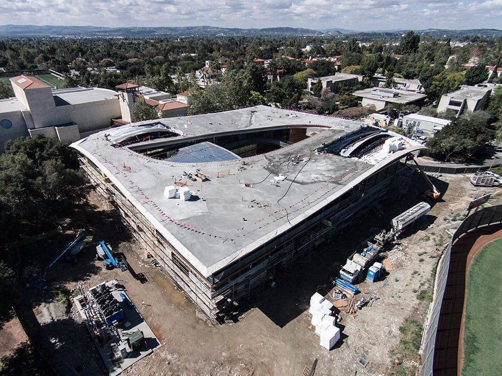 Aerial view of a large, modern building under construction with a central courtyard and a flat, grey roof.