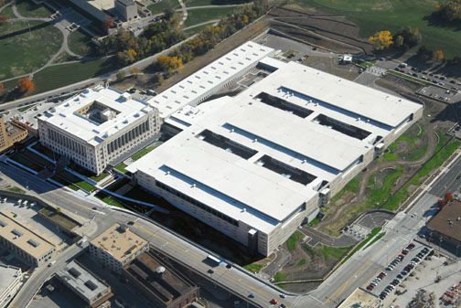 Aerial view of a large white building complex with a historic structure connected to a modern facility near a park.