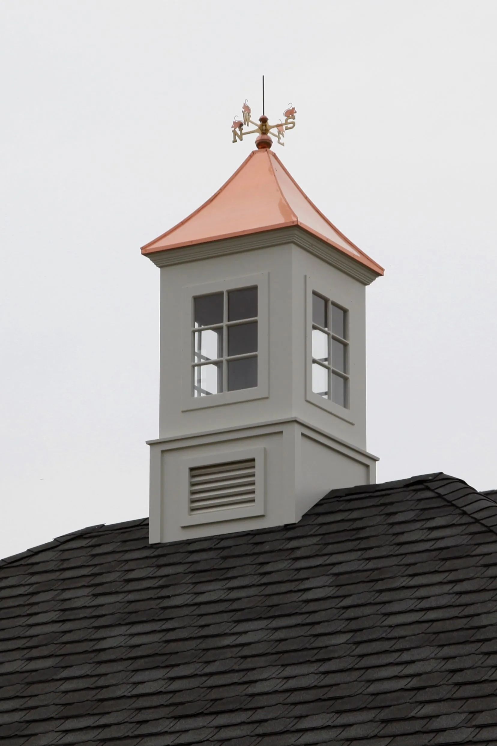 Gray cupola with copper roof and weather vane on a dark roof.