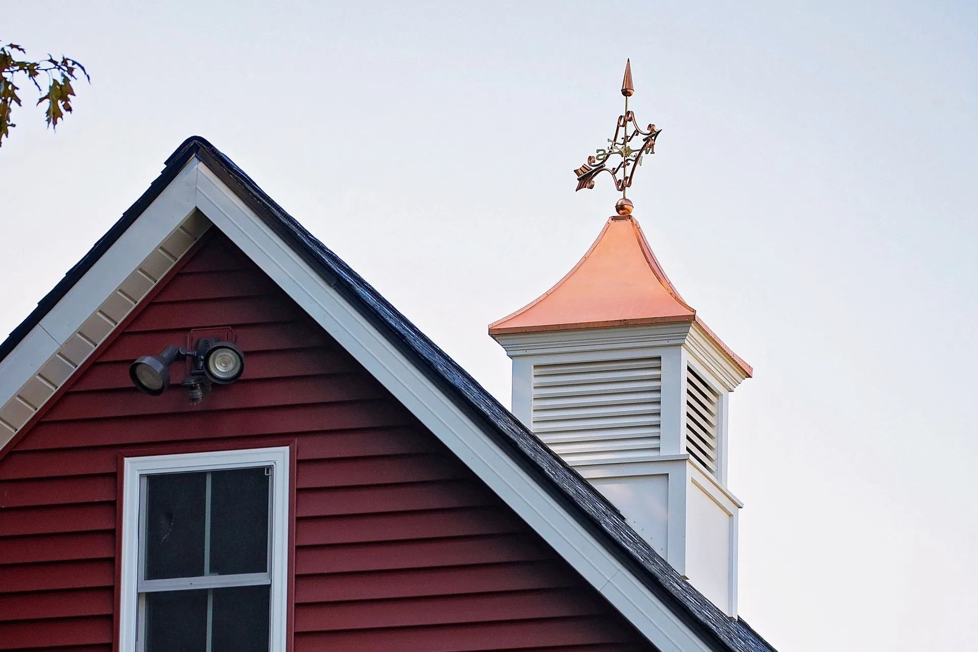 Red barn with white trim and cupola topped with a copper weathervane against a pale blue sky.