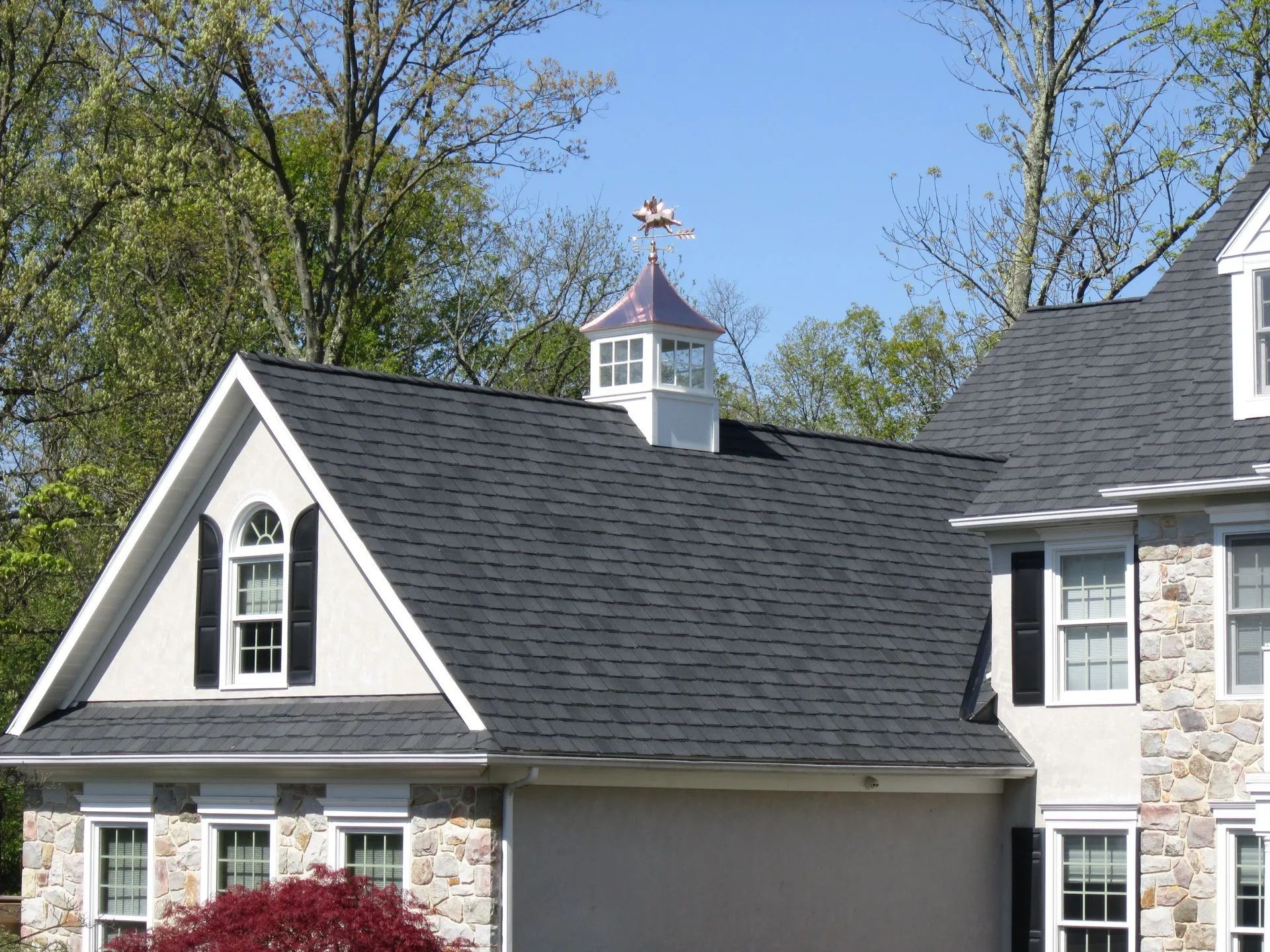 Gray roof with a white cupola and weather vane; building with stone facade.