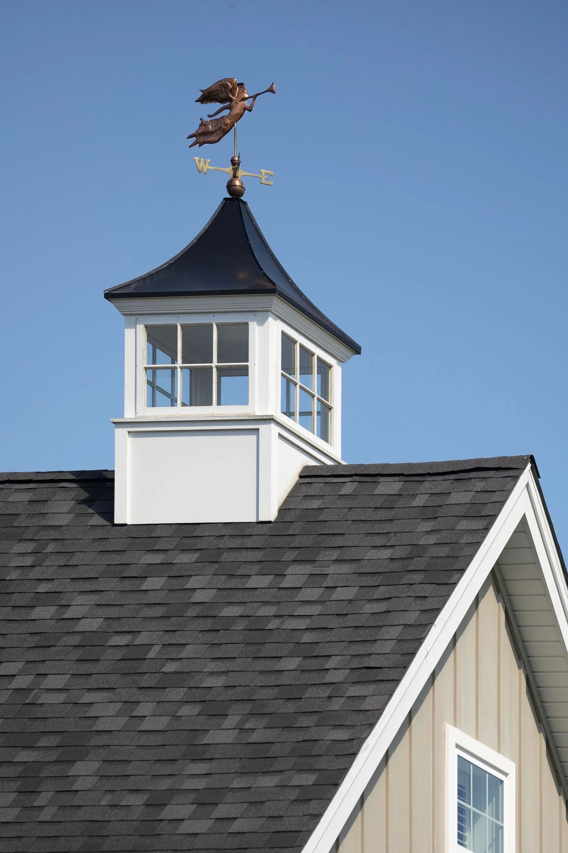 Copper angel weathervane atop a white and black cupola on a gray shingle roof.