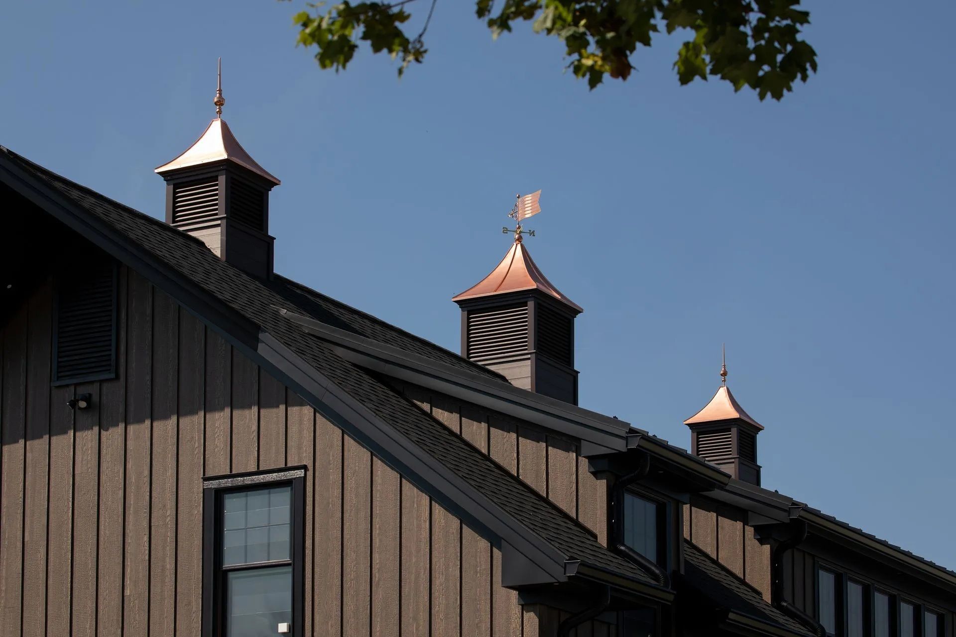Dark brown building with copper-roofed cupolas on a black roof, against a clear blue sky.