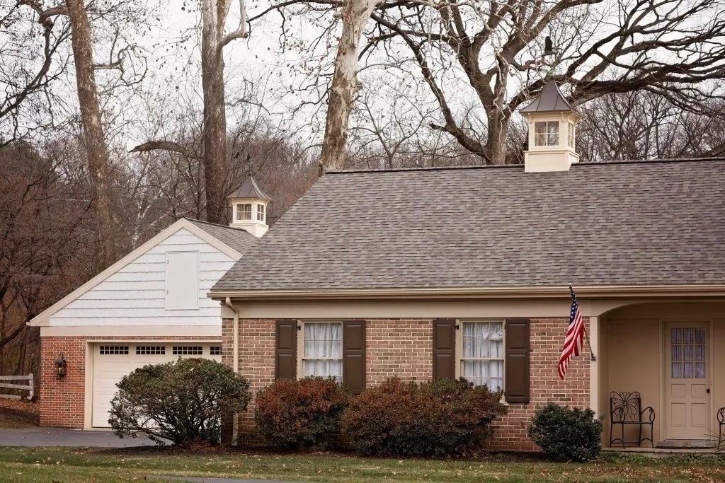 Brick building with garage, shutters, and American flag; trees in background.