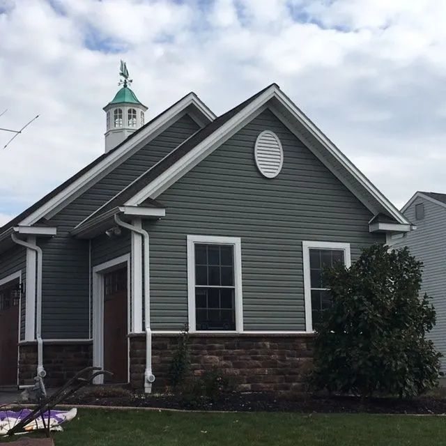 Green siding on a small building with a brick base, white trim, and a cupola topped with a weathervane.