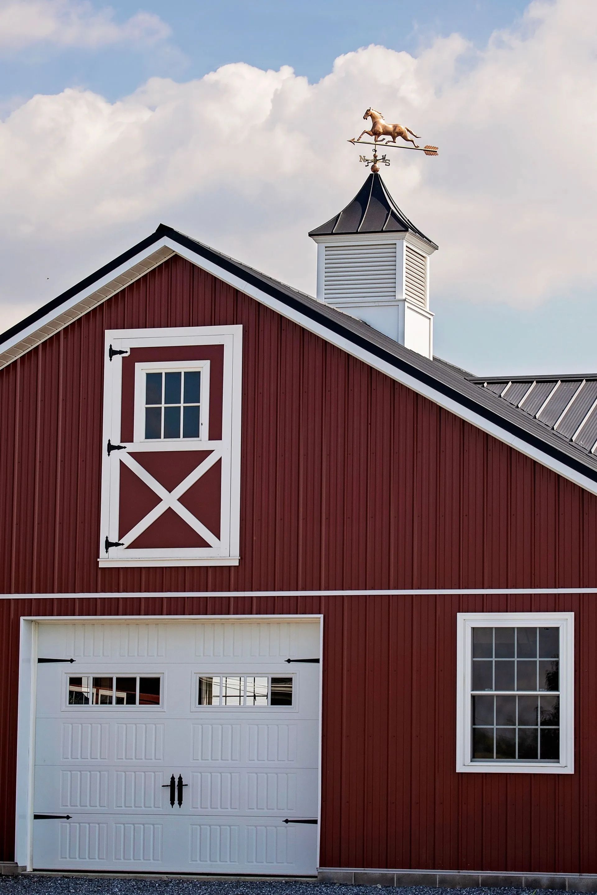 Red barn with white trim, garage door, and a horse weathervane.