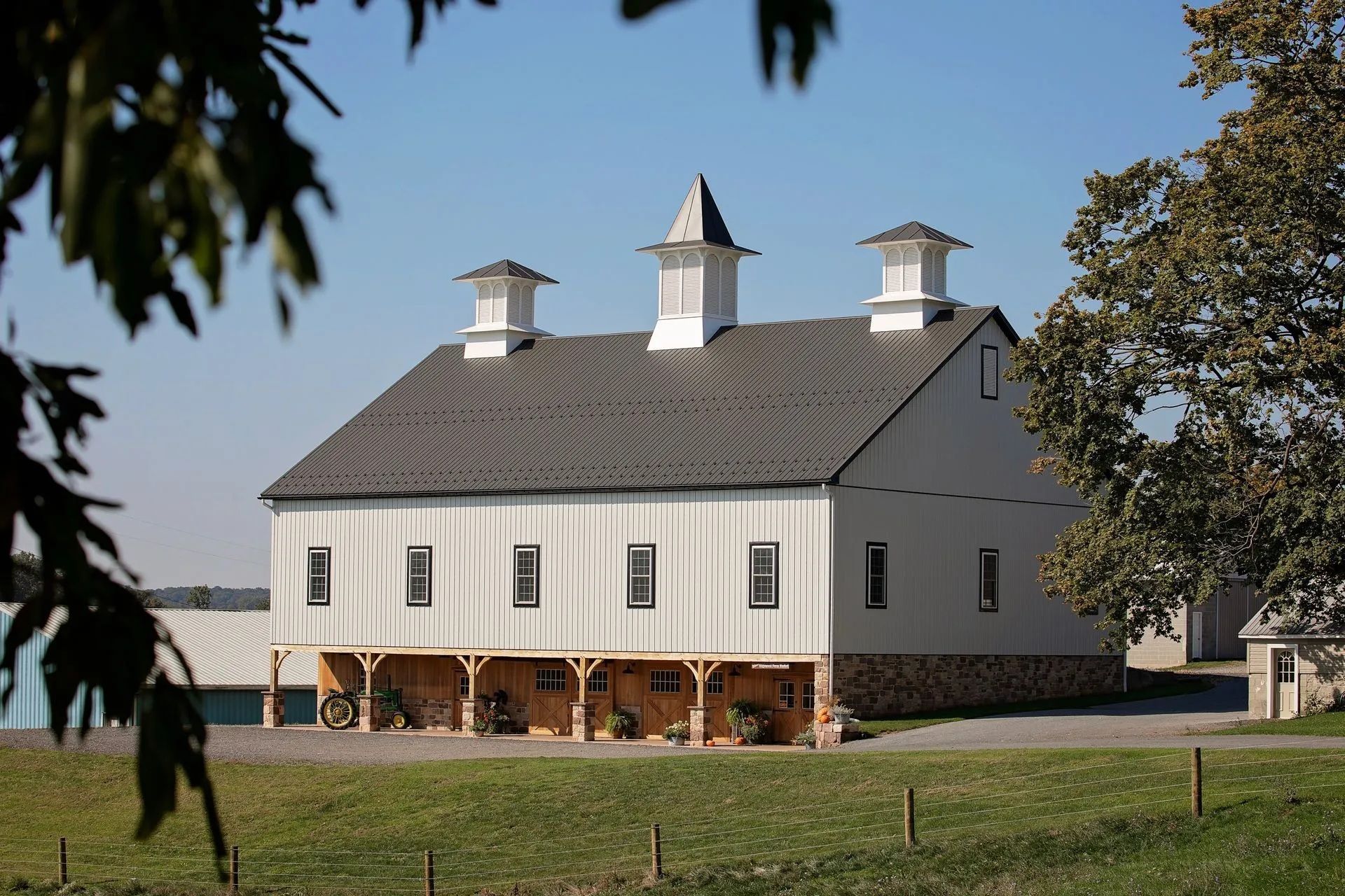 White barn with three cupolas, set on a grassy field on a sunny day.
