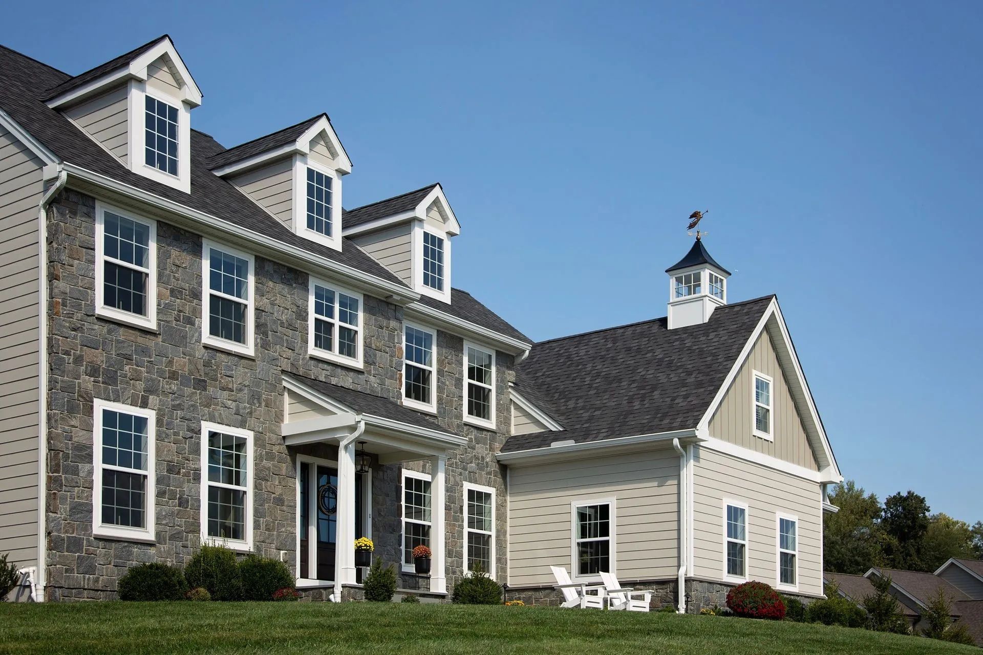 Two-story house with stone and siding facade, dormers, and a small cupola against a blue sky.
