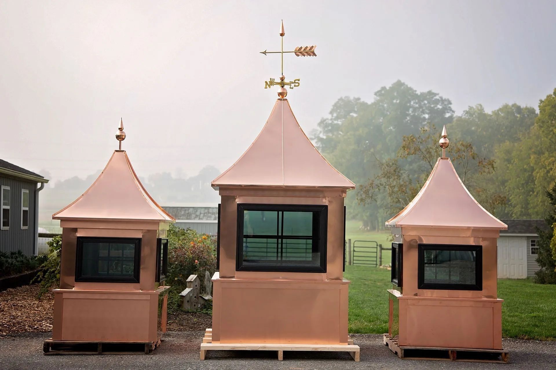 Three copper-roofed structures with windows, one with a weathervane, on a wooden pallet outdoors.