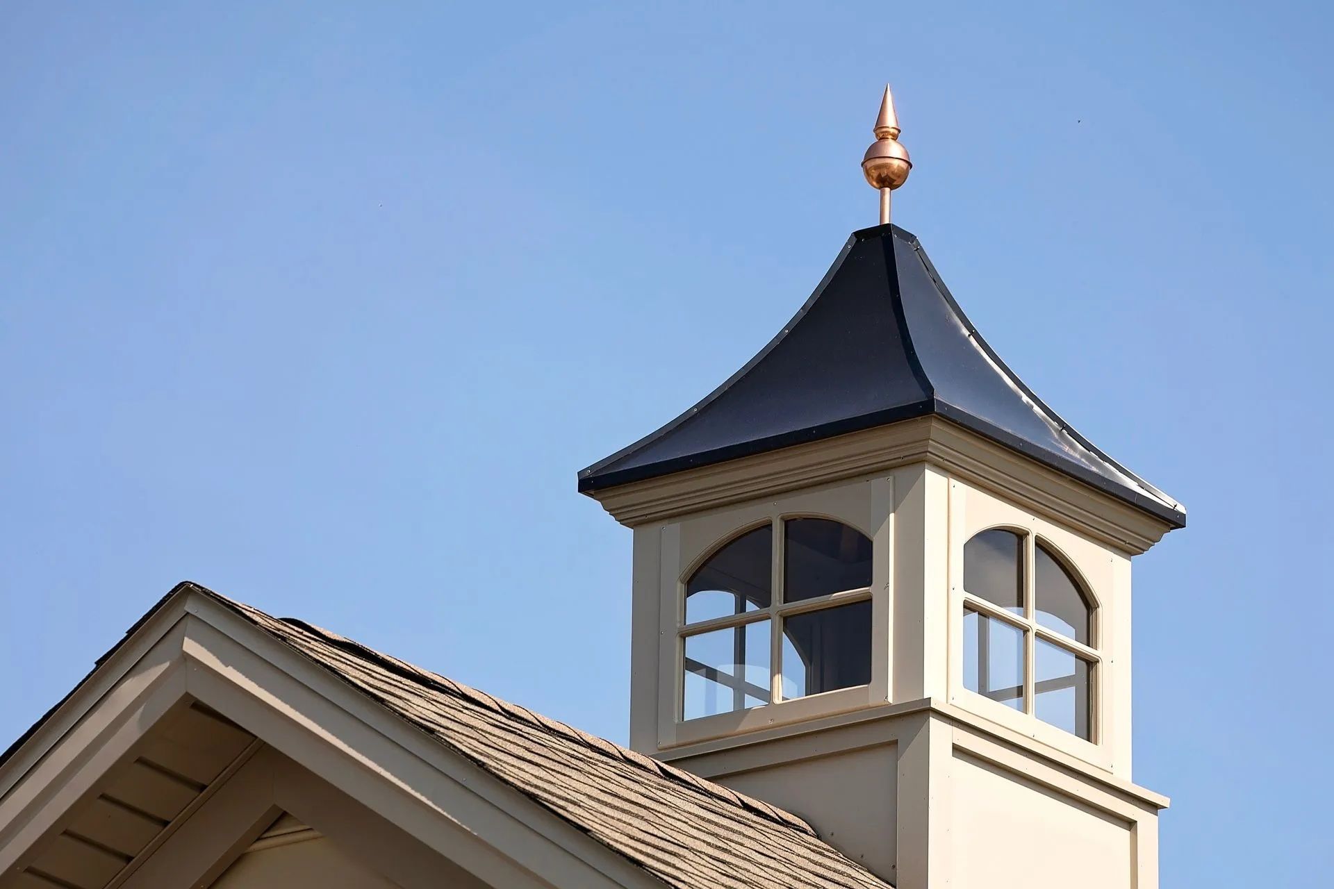 Building turret with black roof and copper finial against a blue sky.