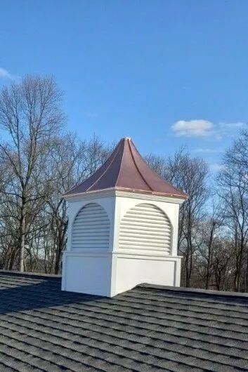 White and copper cupola on a gray shingle roof, set against a blue sky and bare trees.
