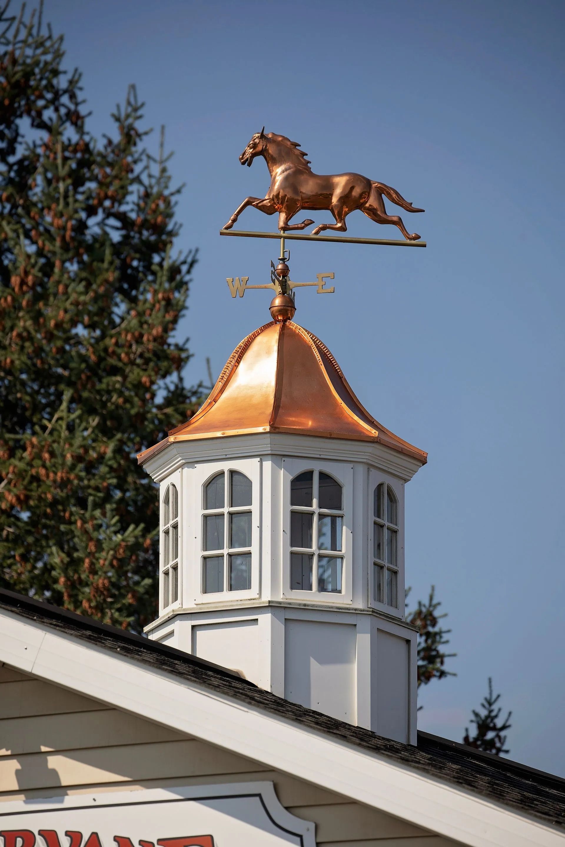 Copper horse weathervane atop a white and copper cupola on a building, against a blue sky.