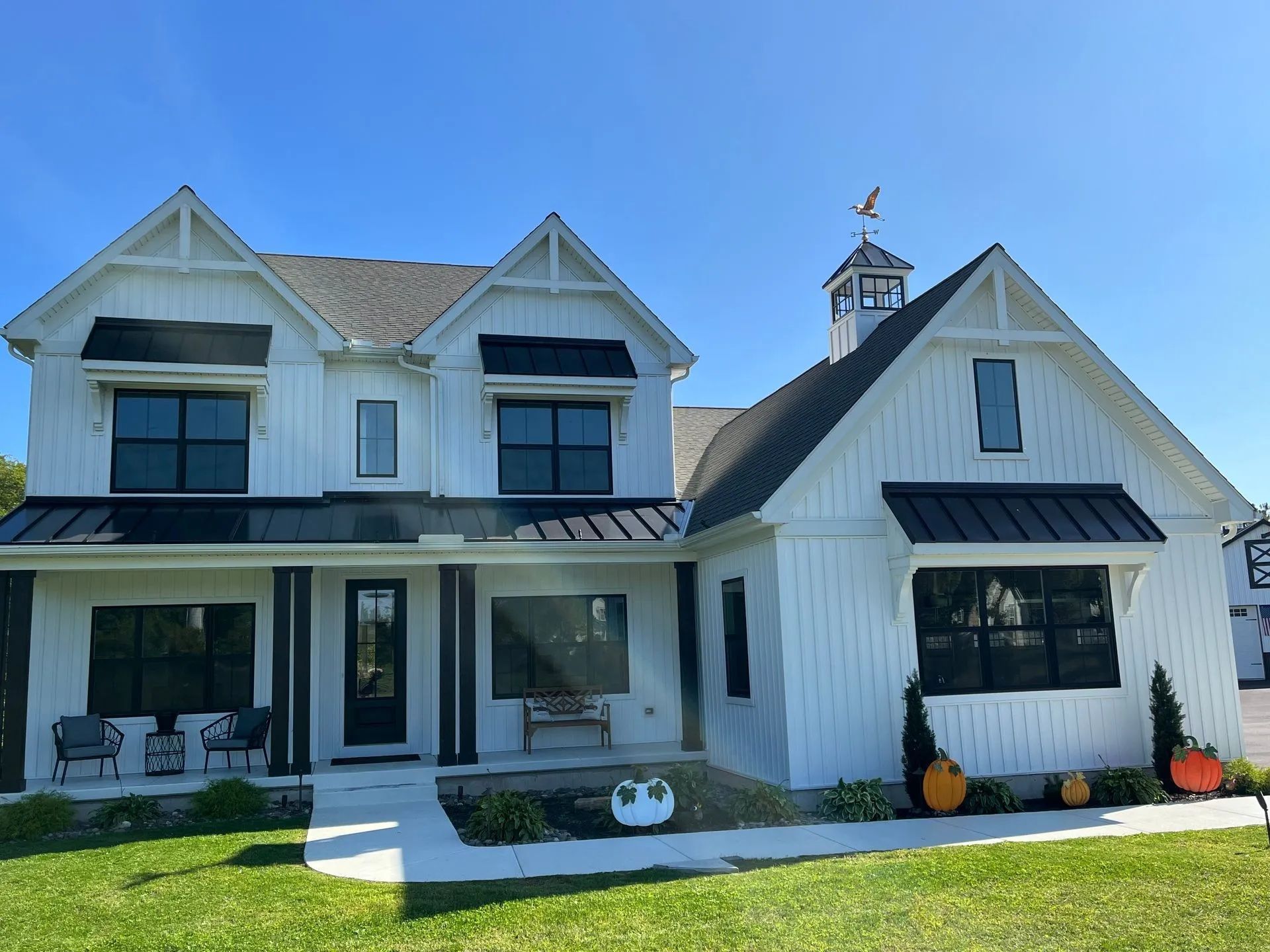 White farmhouse with black accents, blue sky, and pumpkins.
