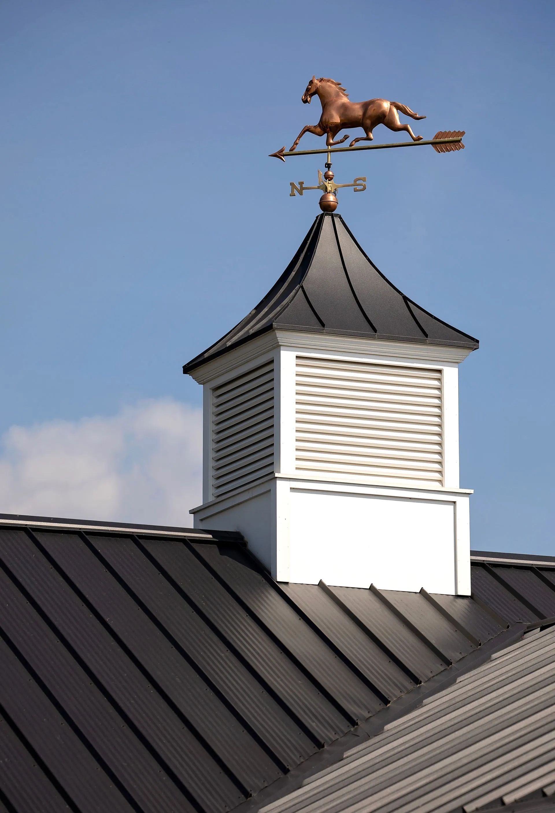 Copper horse weathervane atop a white and black roof with a blue sky background.