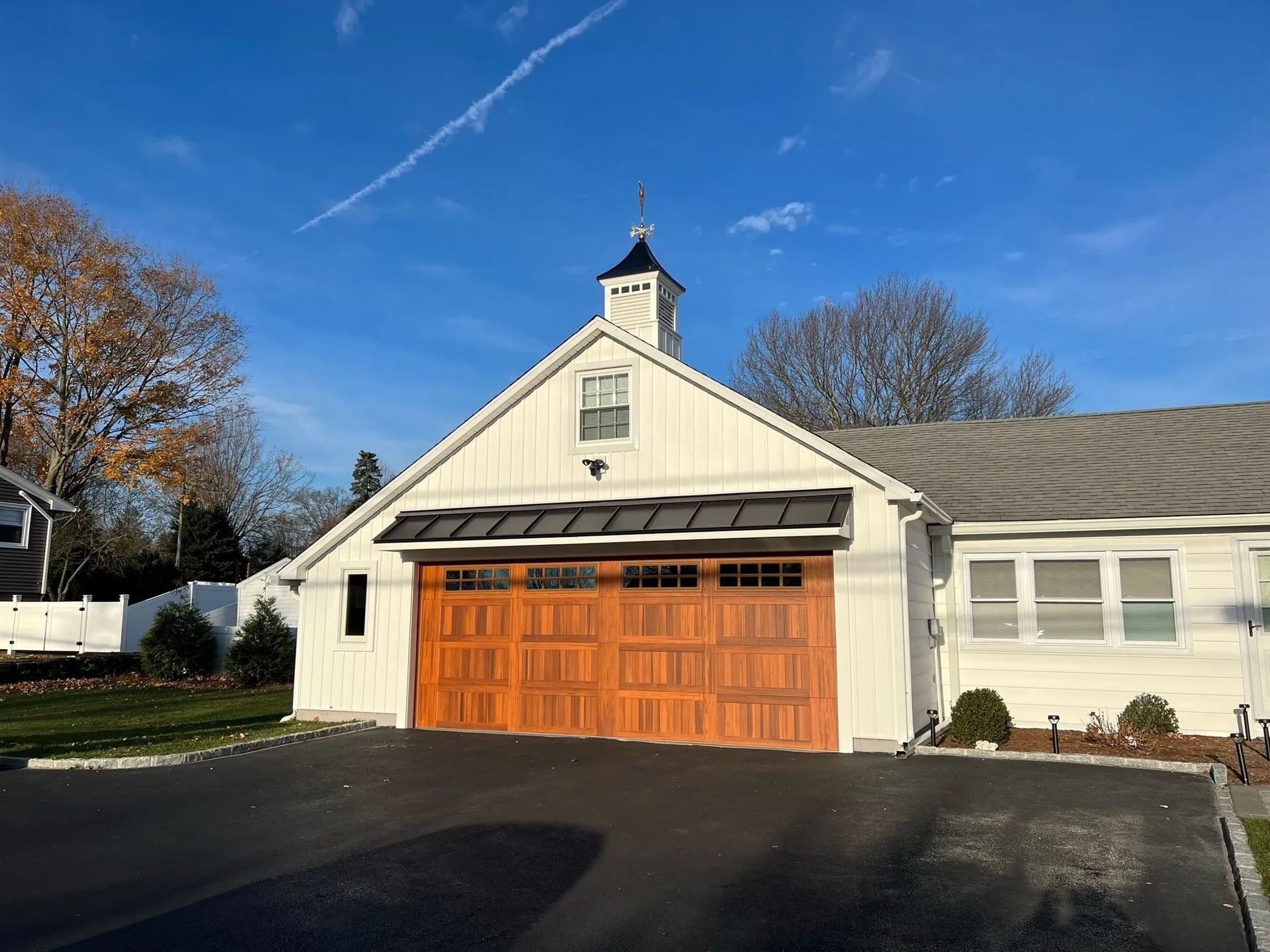 White garage with brown doors, black awning, and a small steeple against a blue sky.